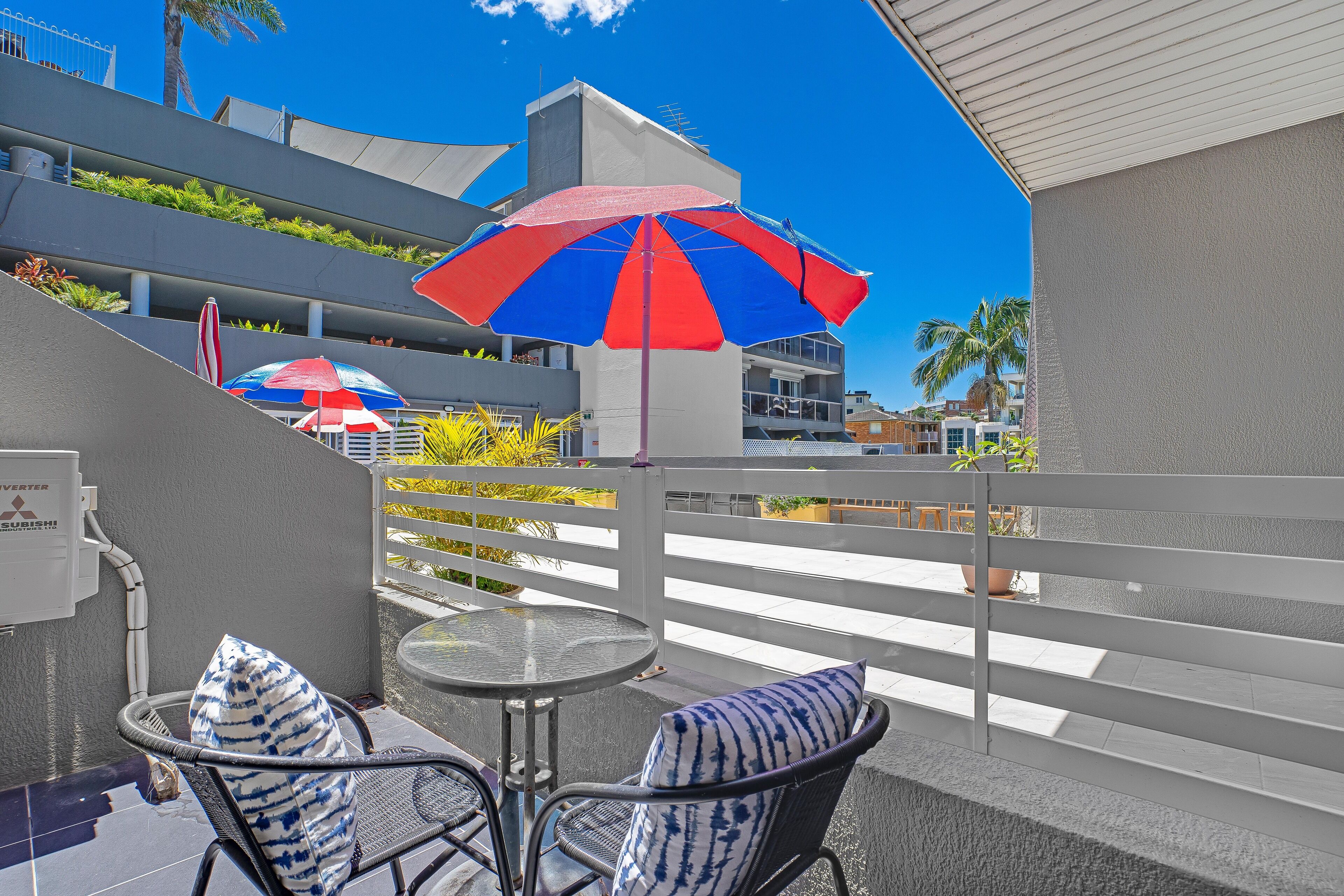 Un balcon avec une table et des chaises, un parasol à rayures et une vue sur des immeubles et des palmiers.