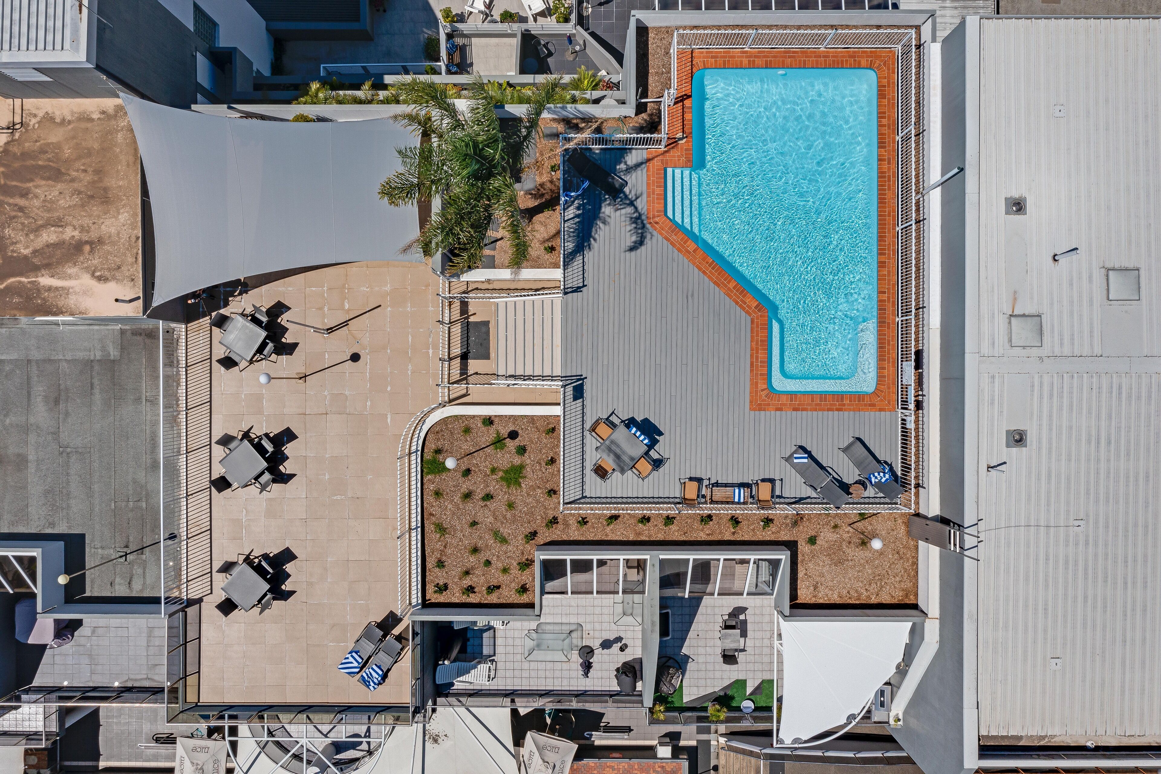An aerial view of a hotel with a swimming pool, outdoor seating, and a patio area.