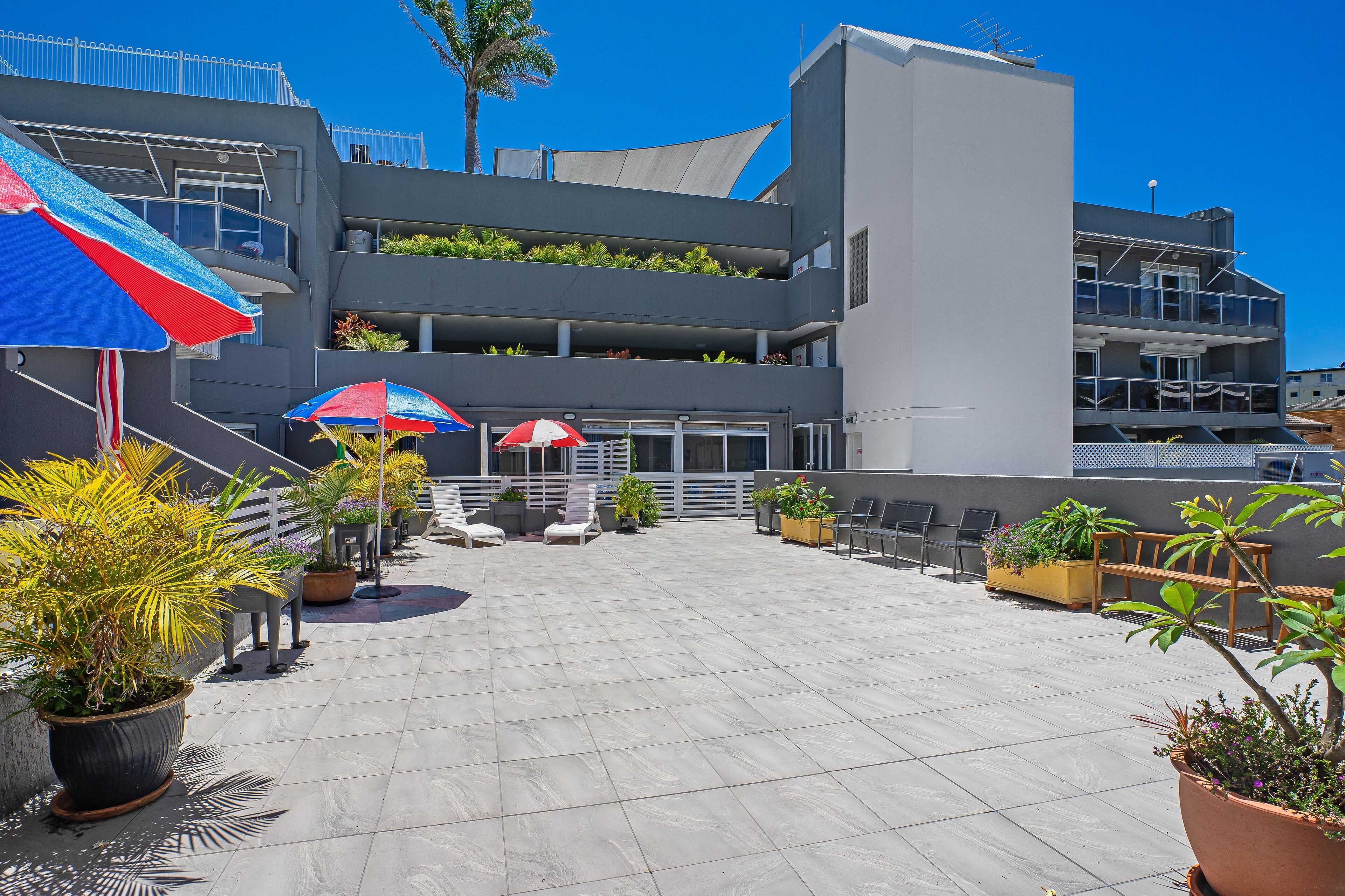 A rooftop patio with potted plants, outdoor seating, and umbrellas.