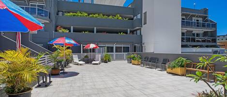 A rooftop patio with potted plants, outdoor seating, and umbrellas.