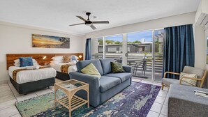 A modern hotel room with a bed, sofa, and armchair, a ceiling fan, and a large window with curtains. - Nelson Towers Motel & Apartments (Nelson Bay)