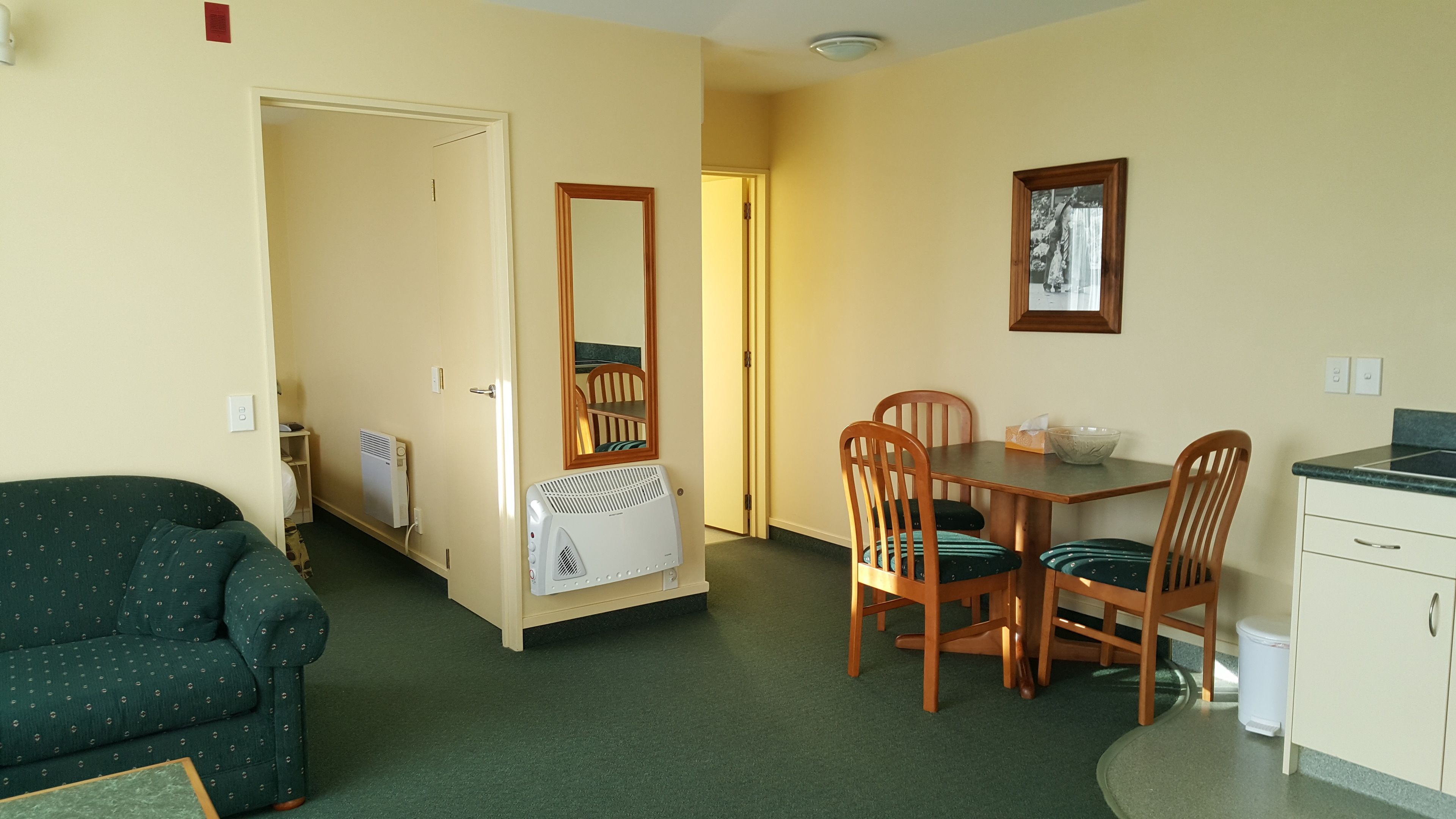 A compact living space with a kitchenette, a dining area with wooden chairs, a green sofa, and a radiator.