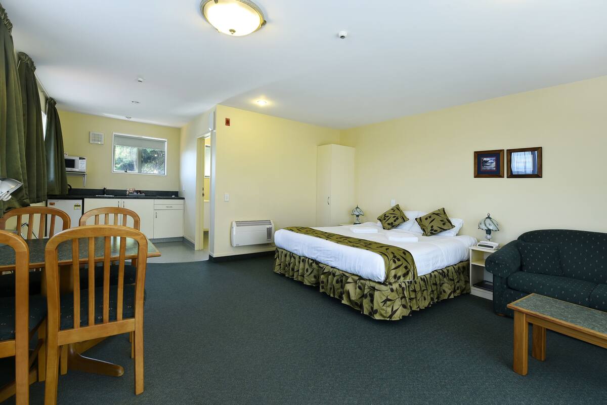 Habitación de hotel con cama, sofá, mesa de comedor con sillas, kitchenette y ventana.