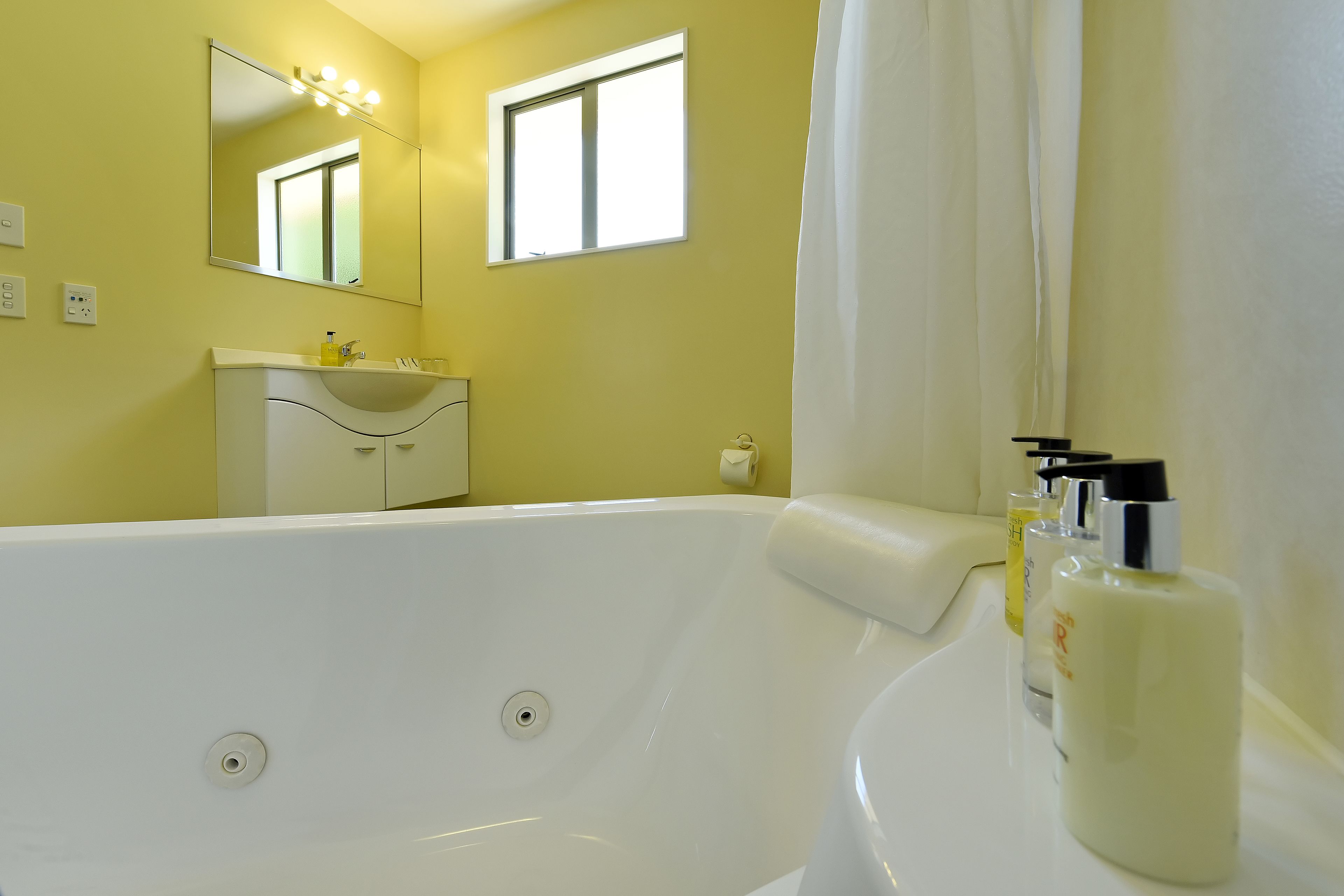 A bathroom with a bathtub, a sink, a mirror, and a window.