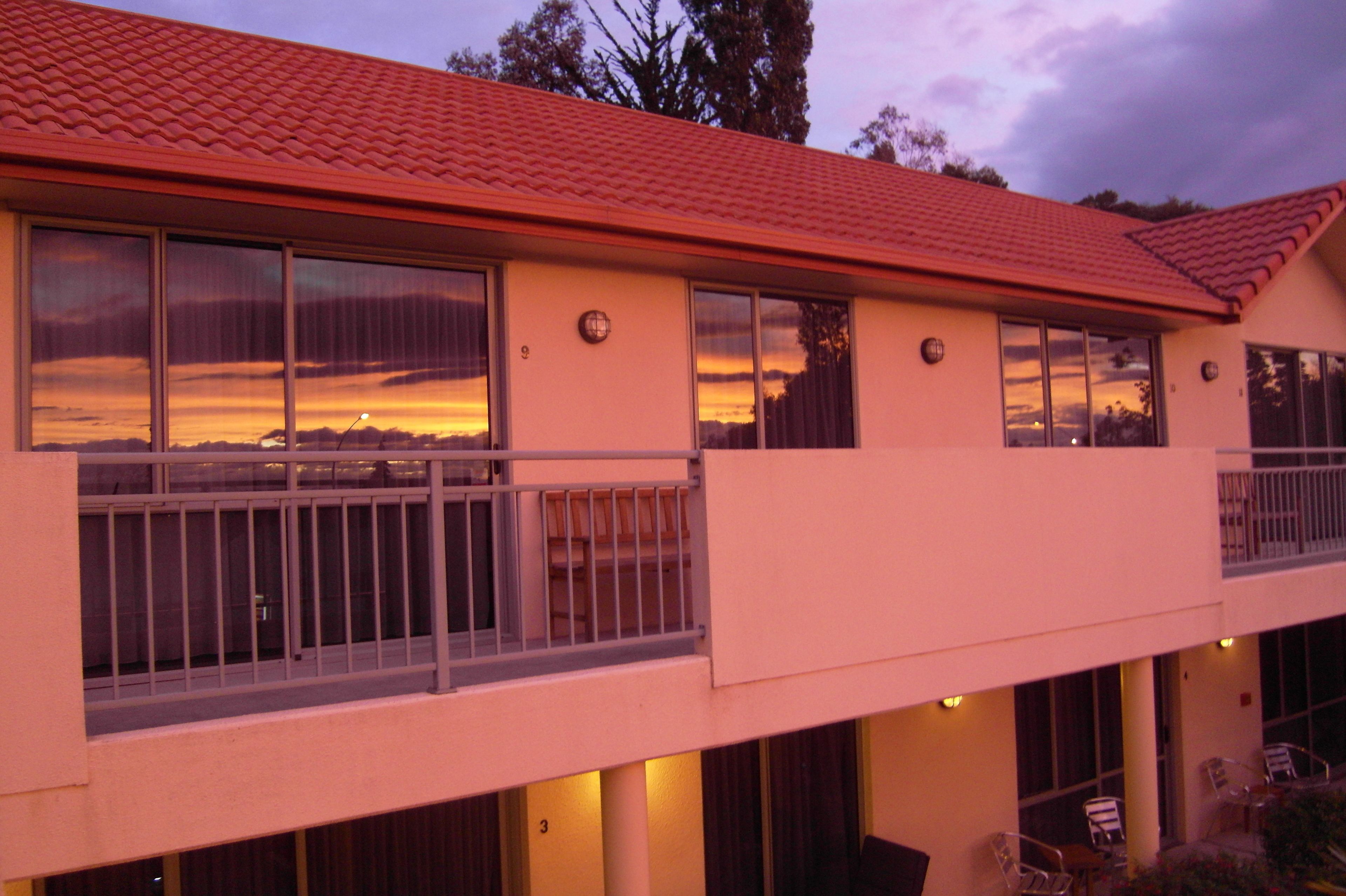 A two-story motel with a red-tiled roof, large windows, and a balcony with metal railings.