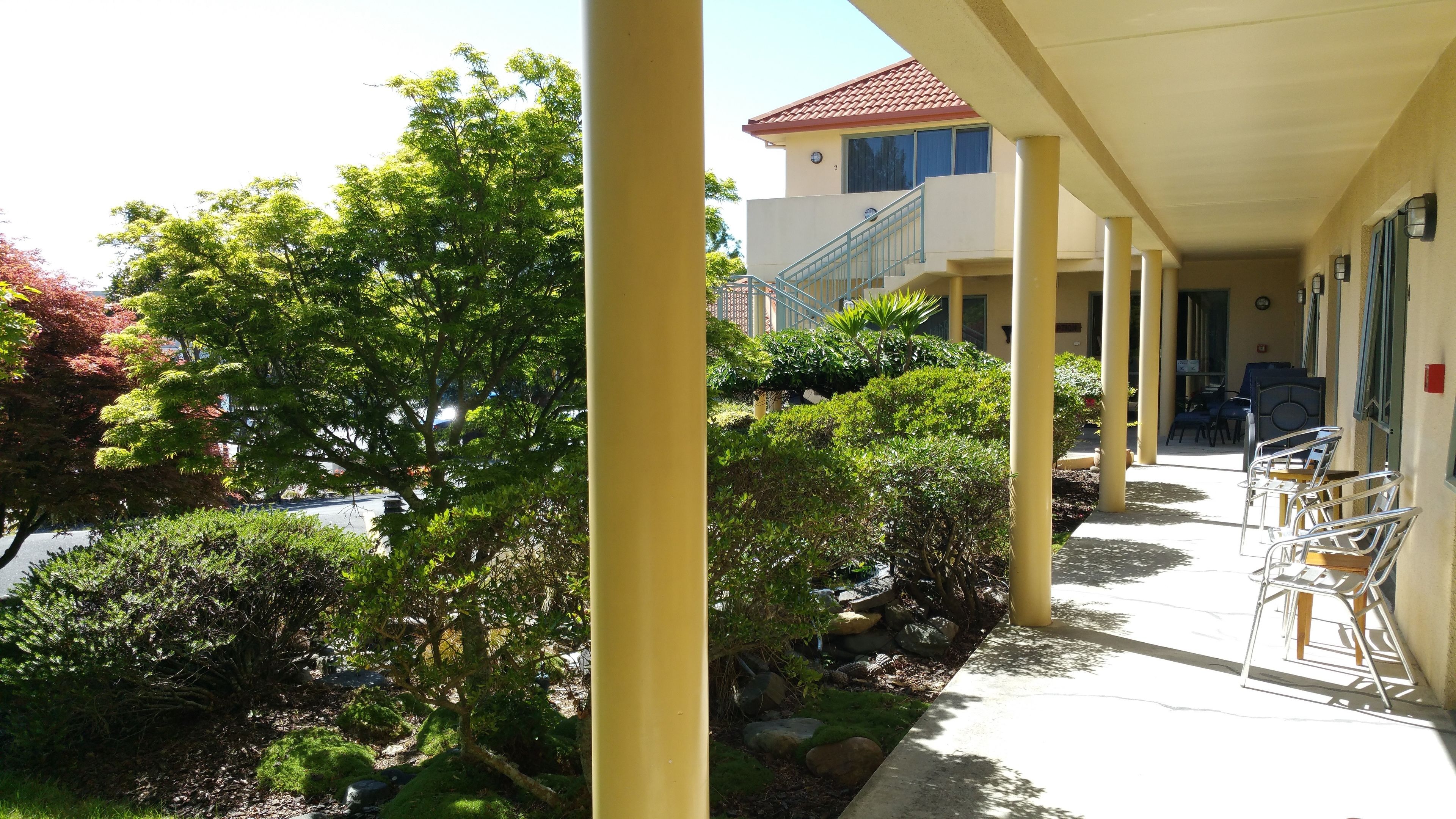 A covered outdoor area with a building in the background, a pathway, and outdoor seating.