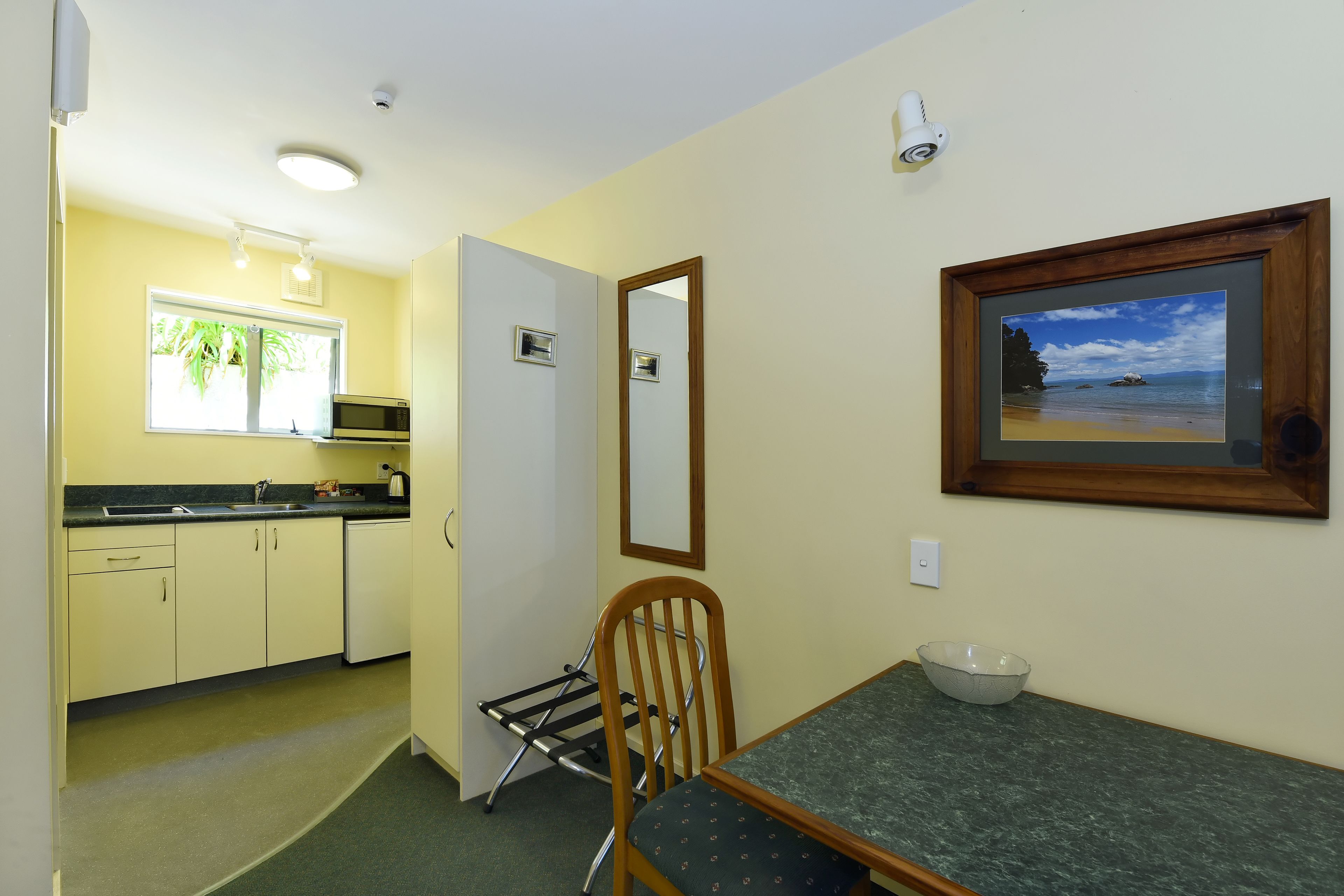 A compact kitchen with a dining area, a microwave, and a framed picture of a beach.
