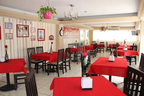 Un restaurante con manteles rojos, sillas de madera y cuadros en las paredes.