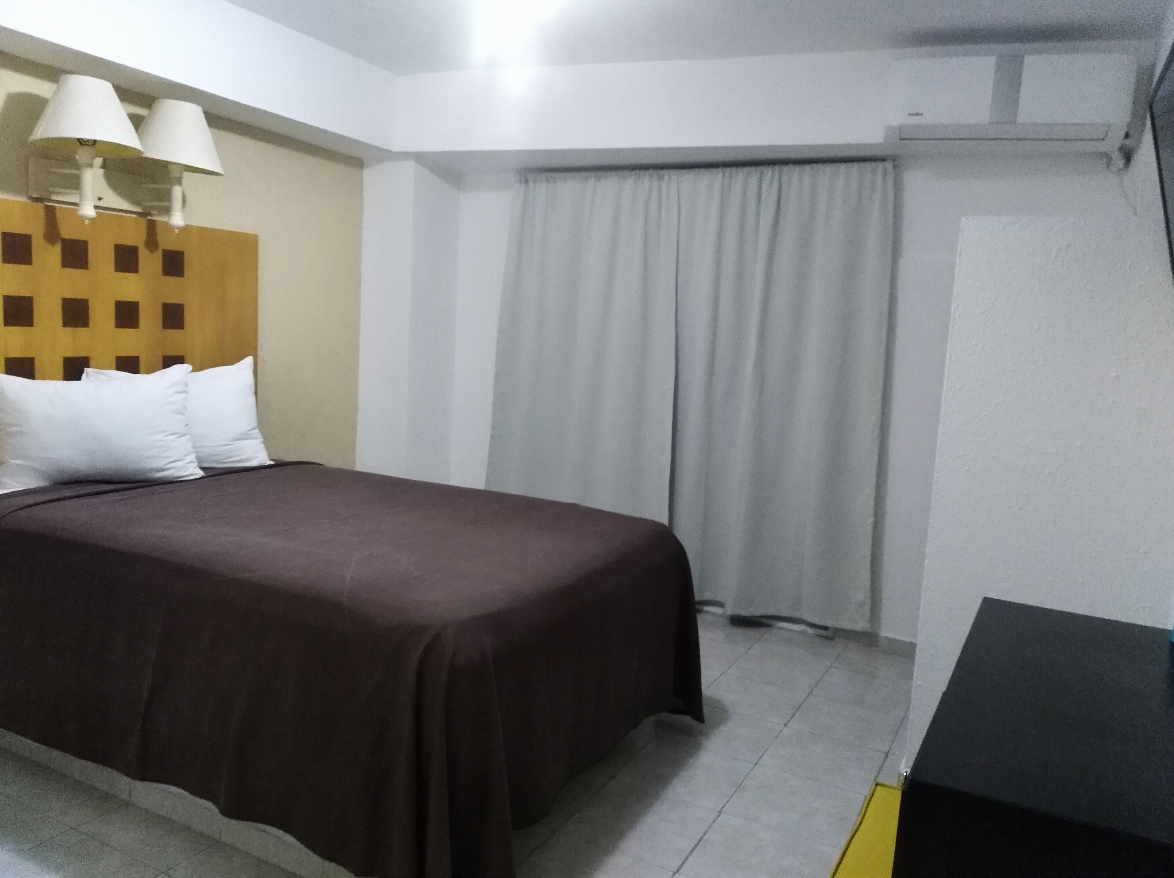 A hotel room with a bed, a headboard, a desk, and a window with curtains.