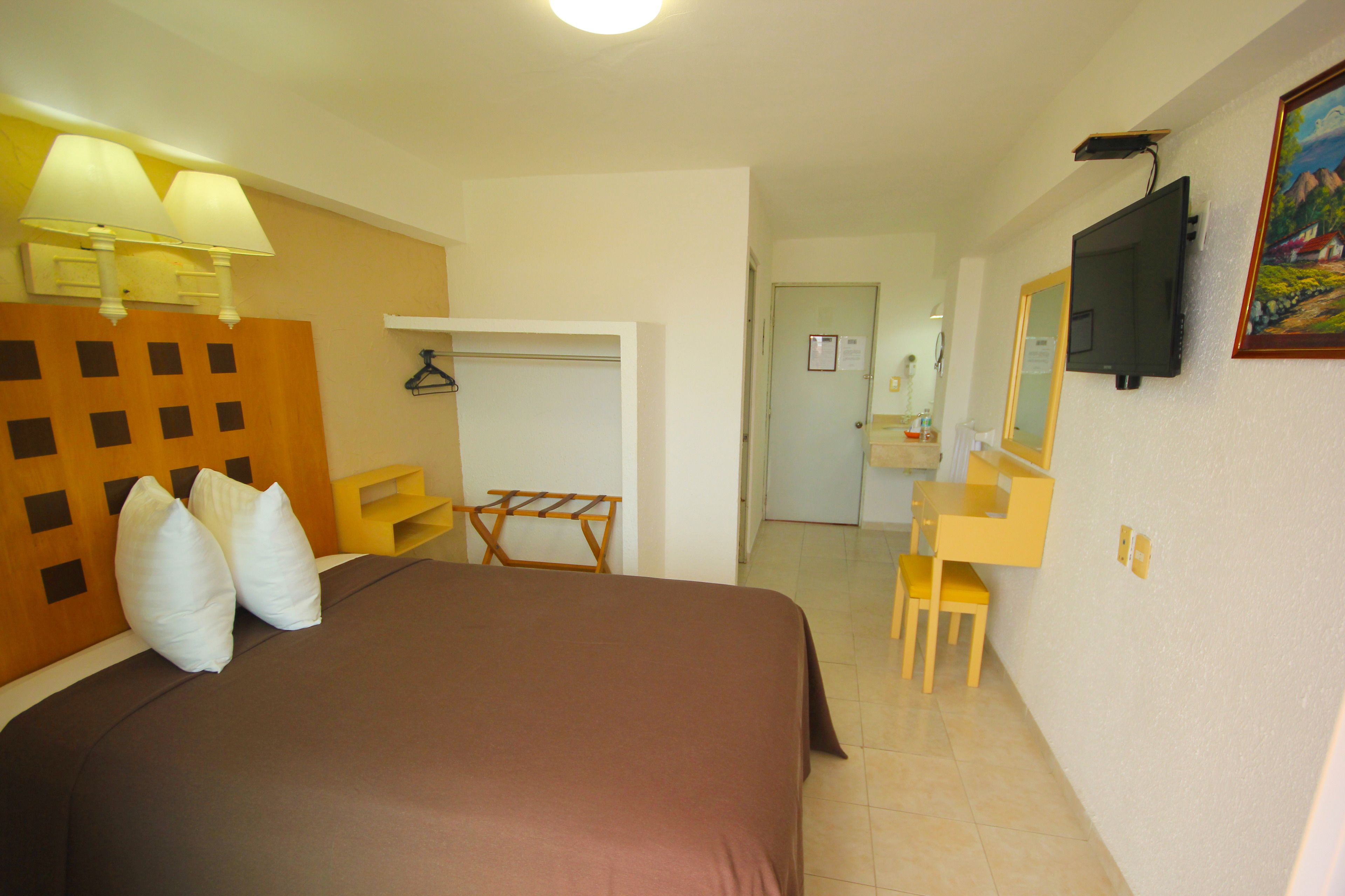 A hotel room with a bed, a desk, a chair, a mirror, and a television.