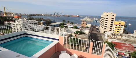 A rooftop pool with a view of the harbor, including ships and cranes.
