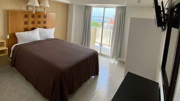A hotel room with a bed, a TV, a desk, and a view of the sea. - Hotel Posada del Carmen (Veracruz)