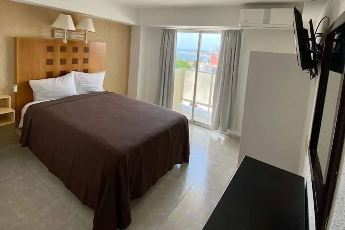 A hotel room with a bed, a TV, a desk, and a view of the sea.