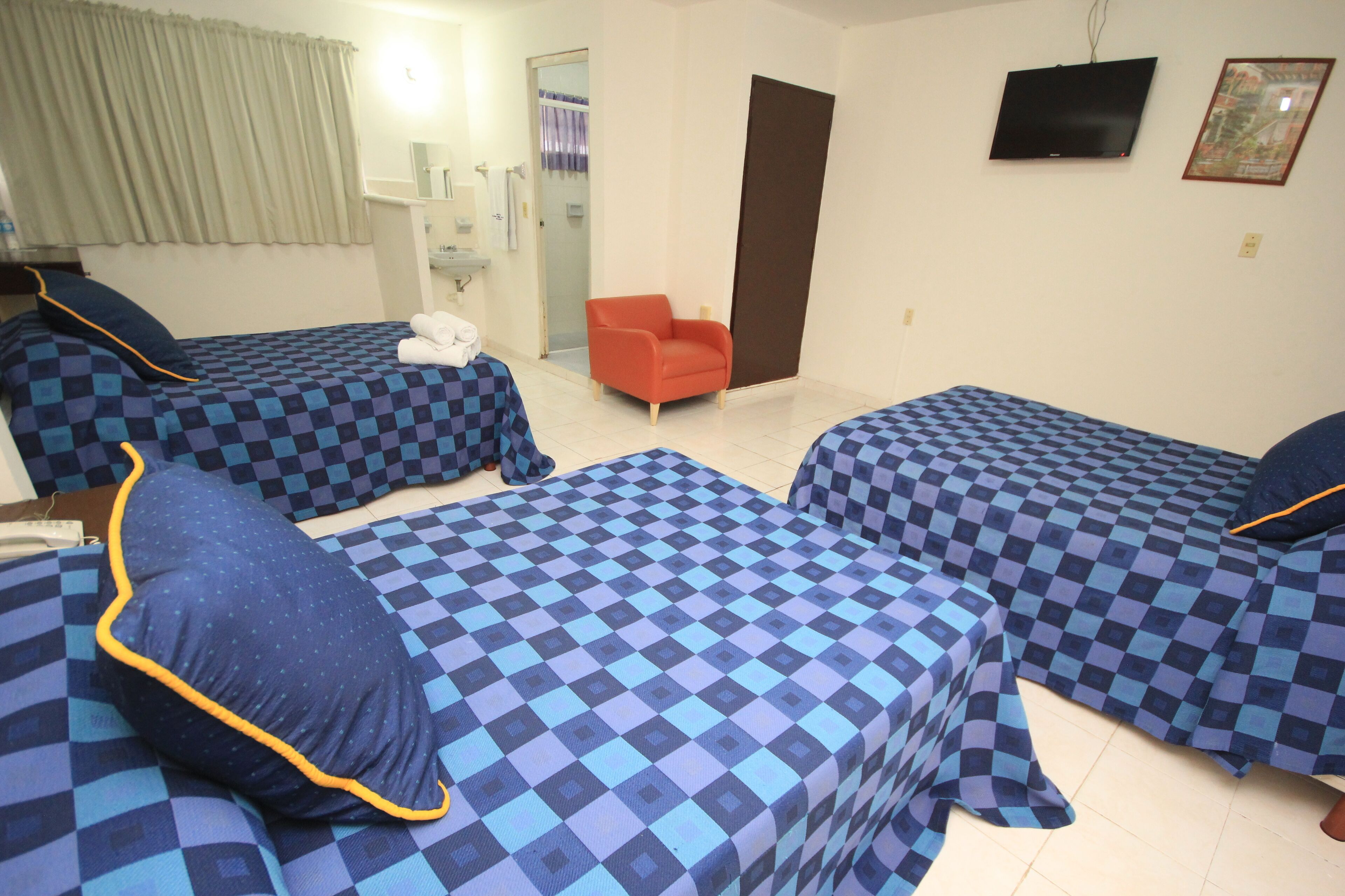A hotel room with two beds, a chair, a TV, and a bathroom visible through an open door.