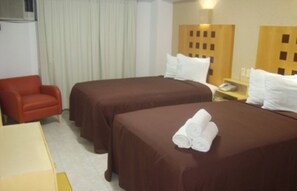 Habitación de hotel con dos camas, un sillón rojo y una mesita de noche con un teléfono.