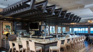 A bar area with a long counter, multiple bar stools, and a television mounted on the wall. - Cape Rey Carlsbad Beach, a Hilton Resort & Spa (Carlsbad)