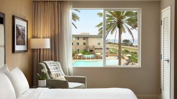 A hotel room with a bed, a chair, a window with a view of a pool and palm trees, and a door.