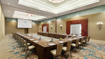 A conference room with a long table, chairs, a projector screen, and a carpeted floor.