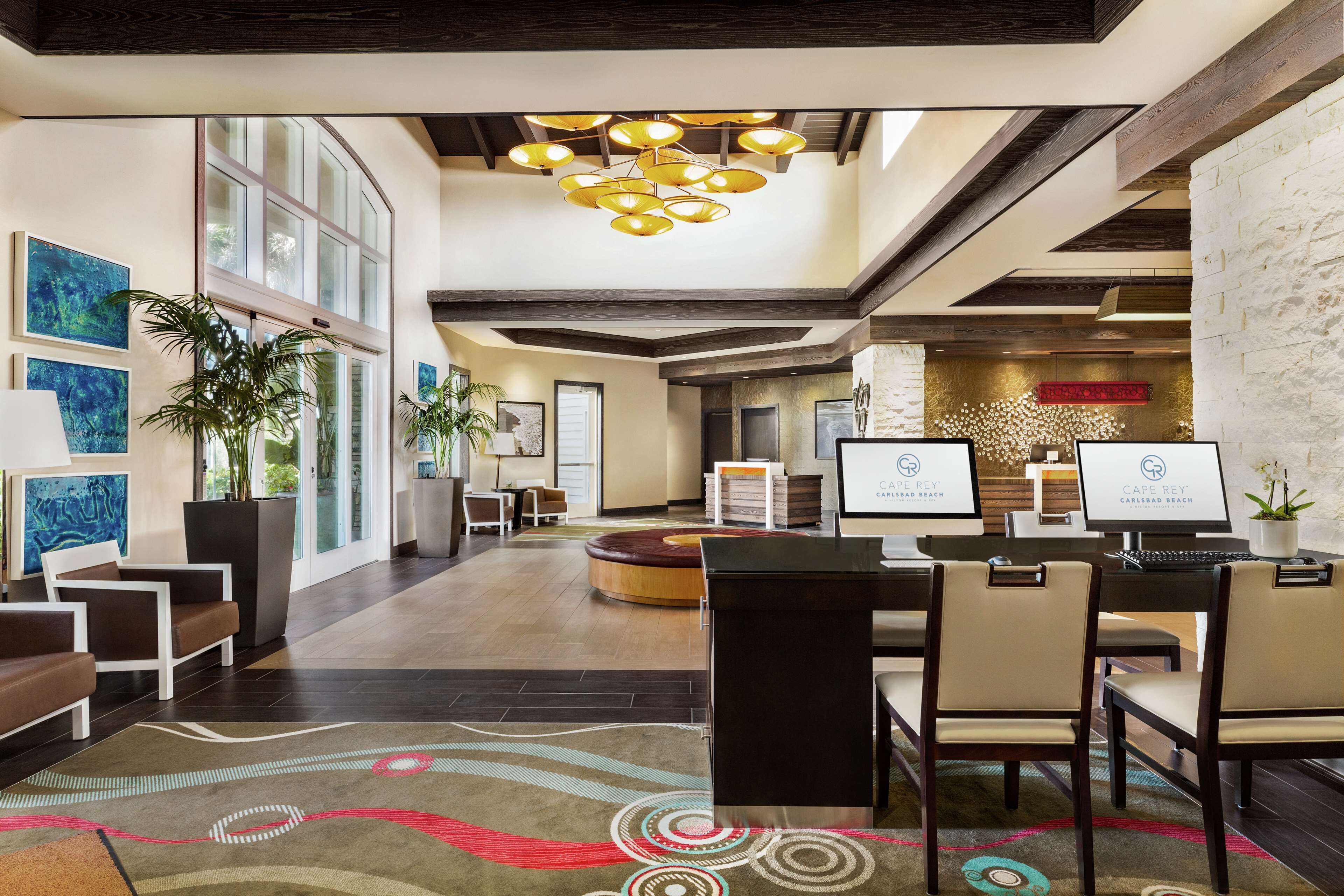 A hotel lobby with a reception desk, seating area, and large windows.