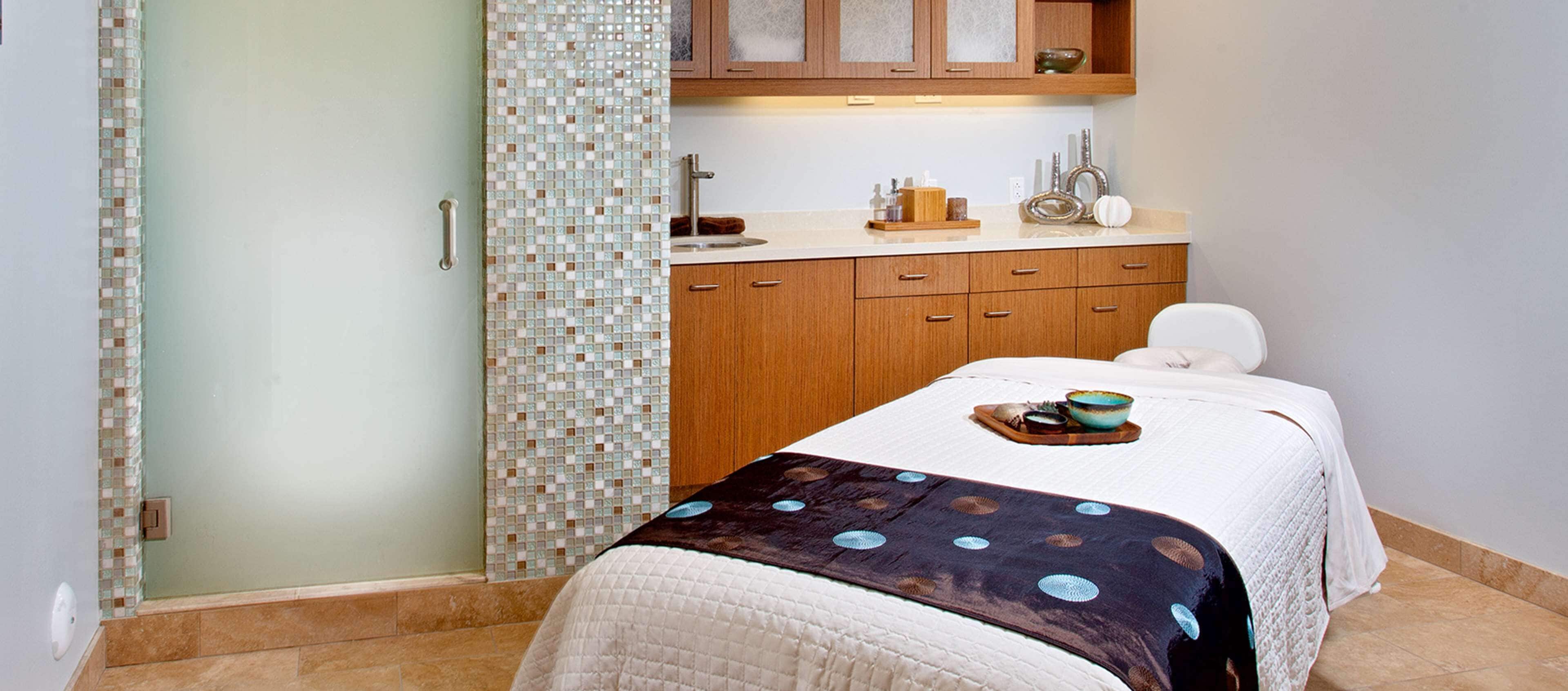 A bedroom with a bed, a bedside table, a nightstand, a window, and a bathroom with a shower and a toilet.