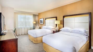 A hotel room with two beds, a desk, a chair, and a television.