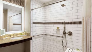 A bathroom with white tiled walls, a granite countertop, a sink, a mirror, a shower with a handheld showerhead, and a towel rack.