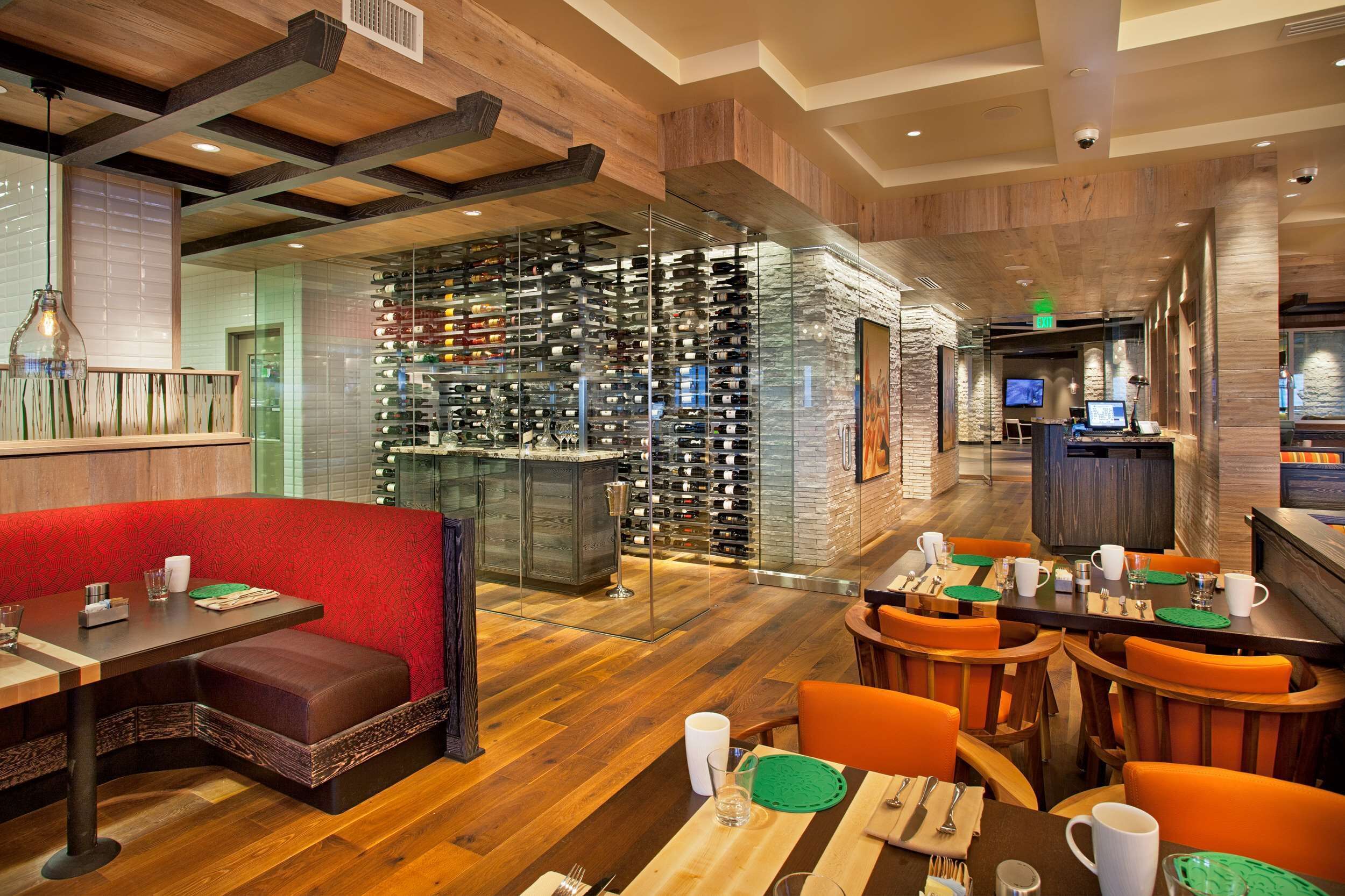 Un restaurante con suelos de madera, asientos rojos y una estantería para vinos.