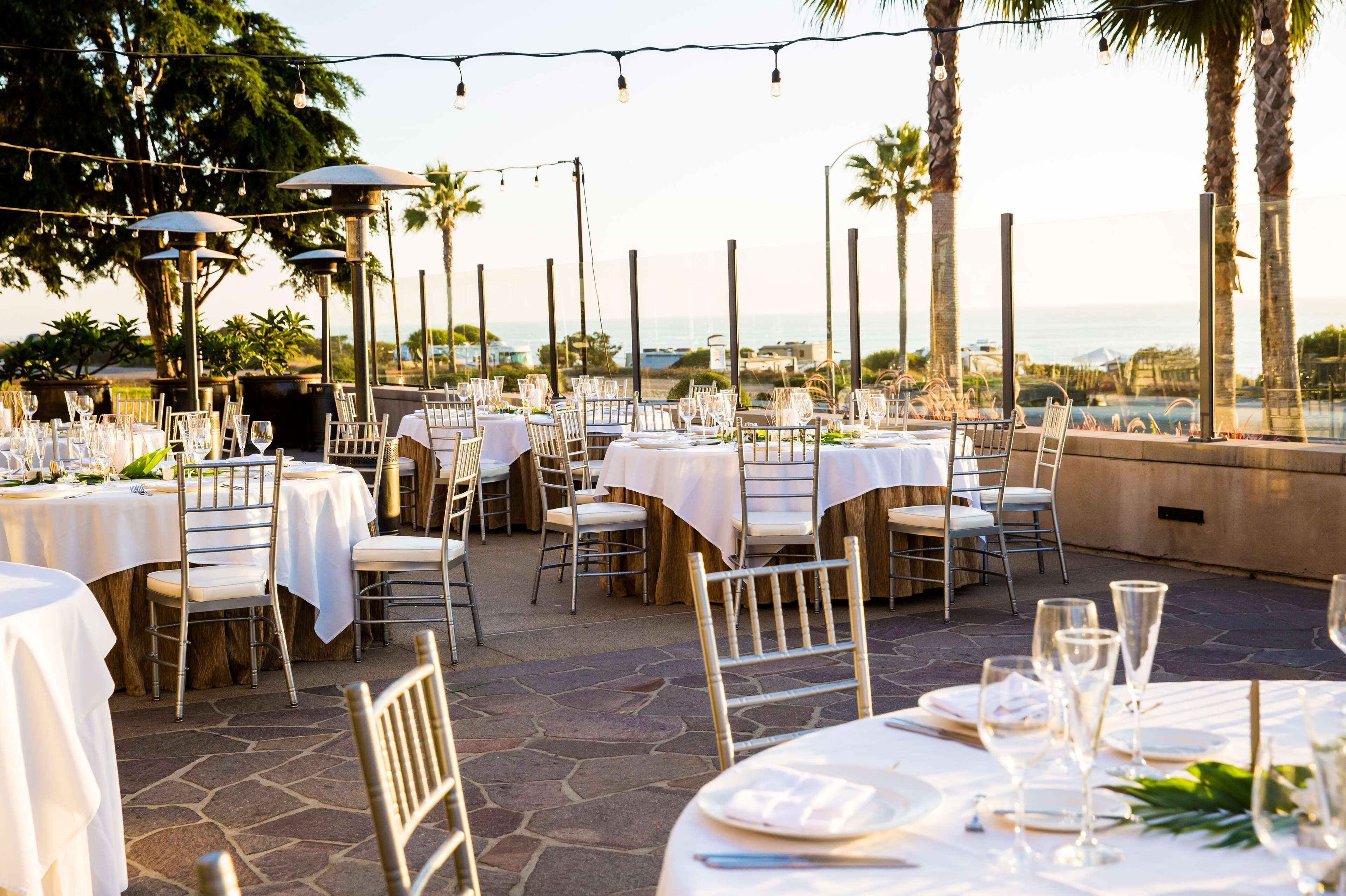 An outdoor dining area with round tables, chairs, and string lights.