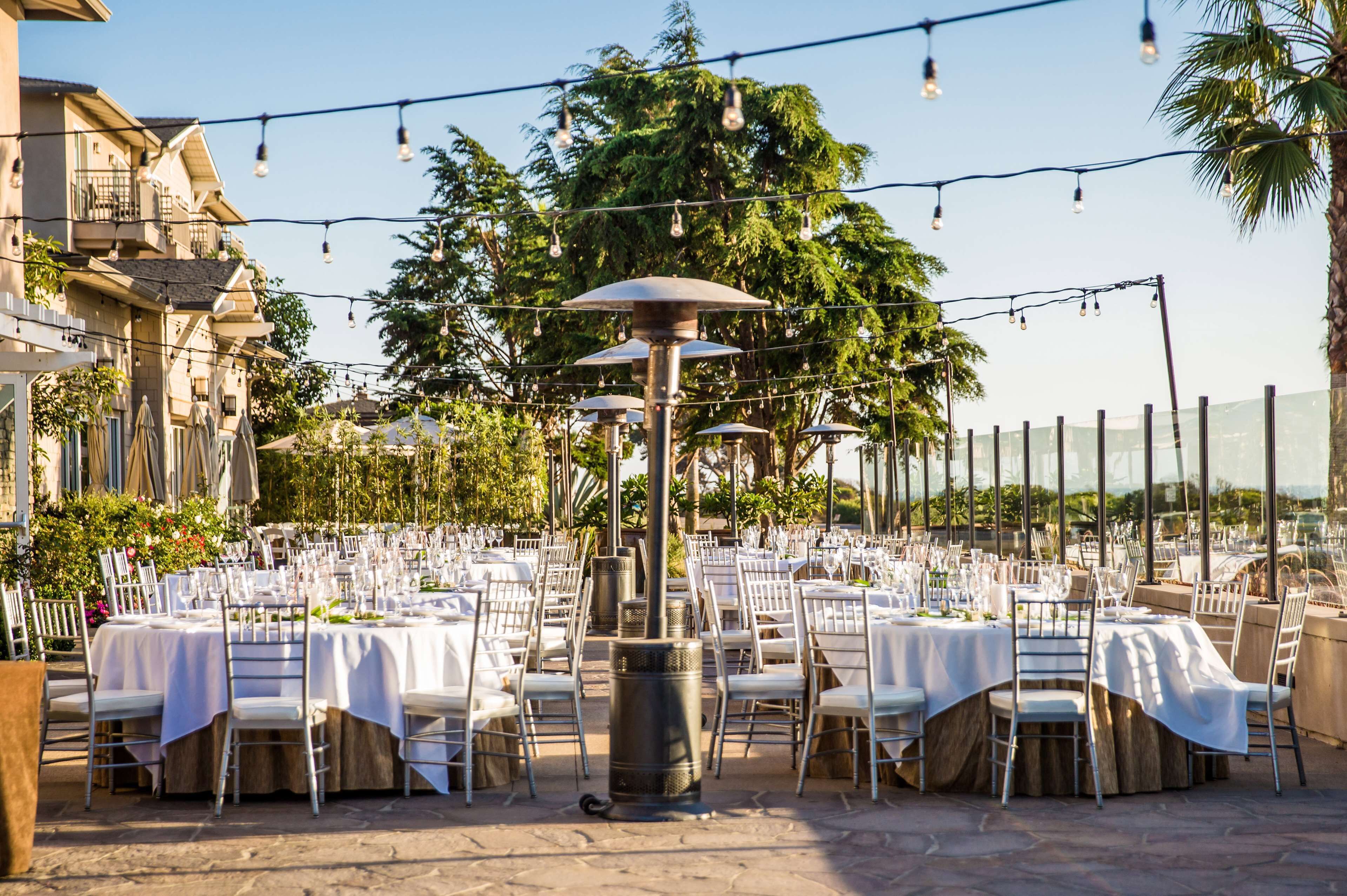 An outdoor dining area with multiple tables set for guests, surrounded by trees and buildings.