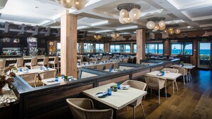A restaurant with high wooden ceilings, multiple seating areas, and large windows offering a view of the ocean. - Cape Rey Carlsbad Beach, a Hilton Resort & Spa (Carlsbad)