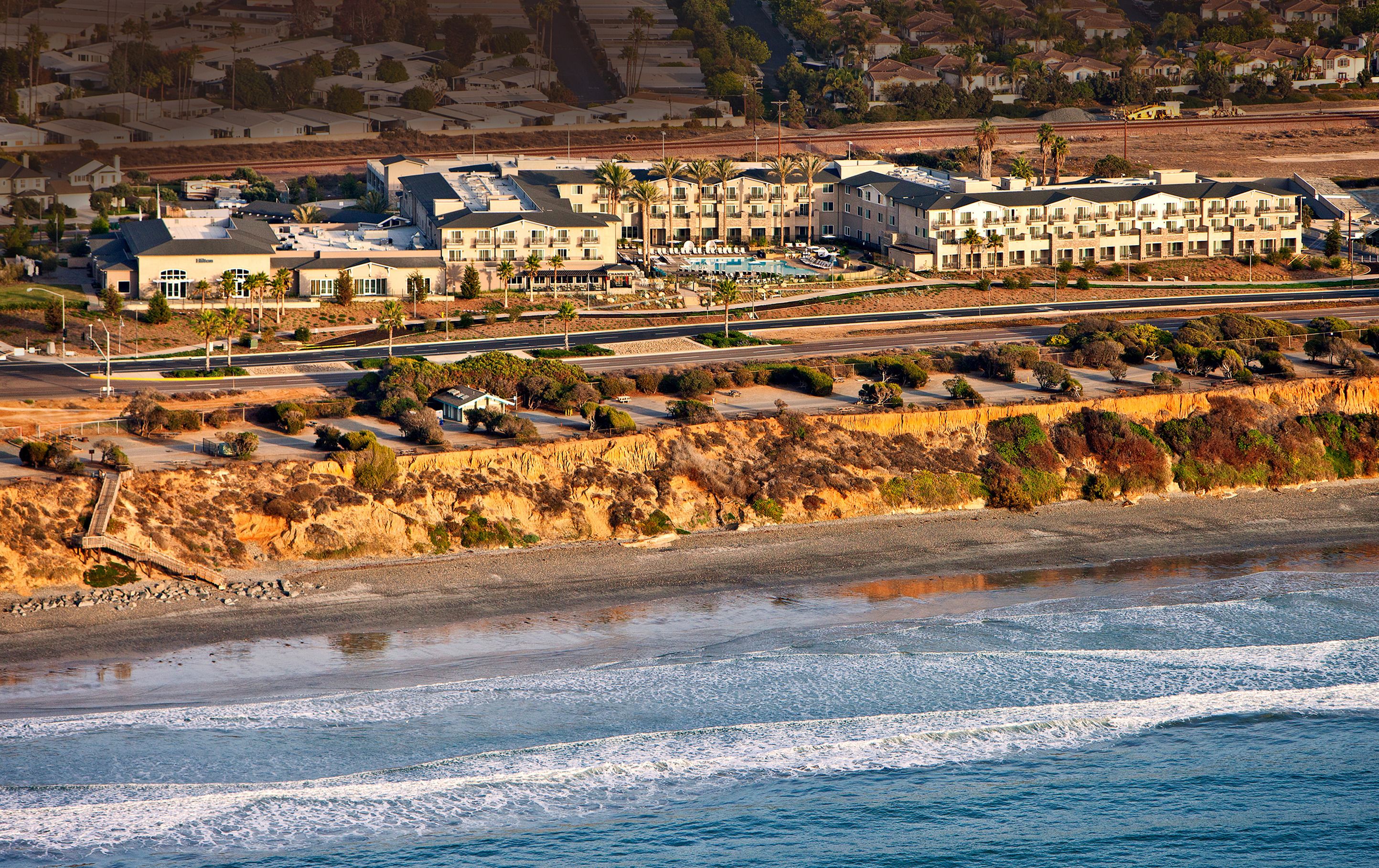 A coastal hotel with multiple buildings, a beach, and a road.