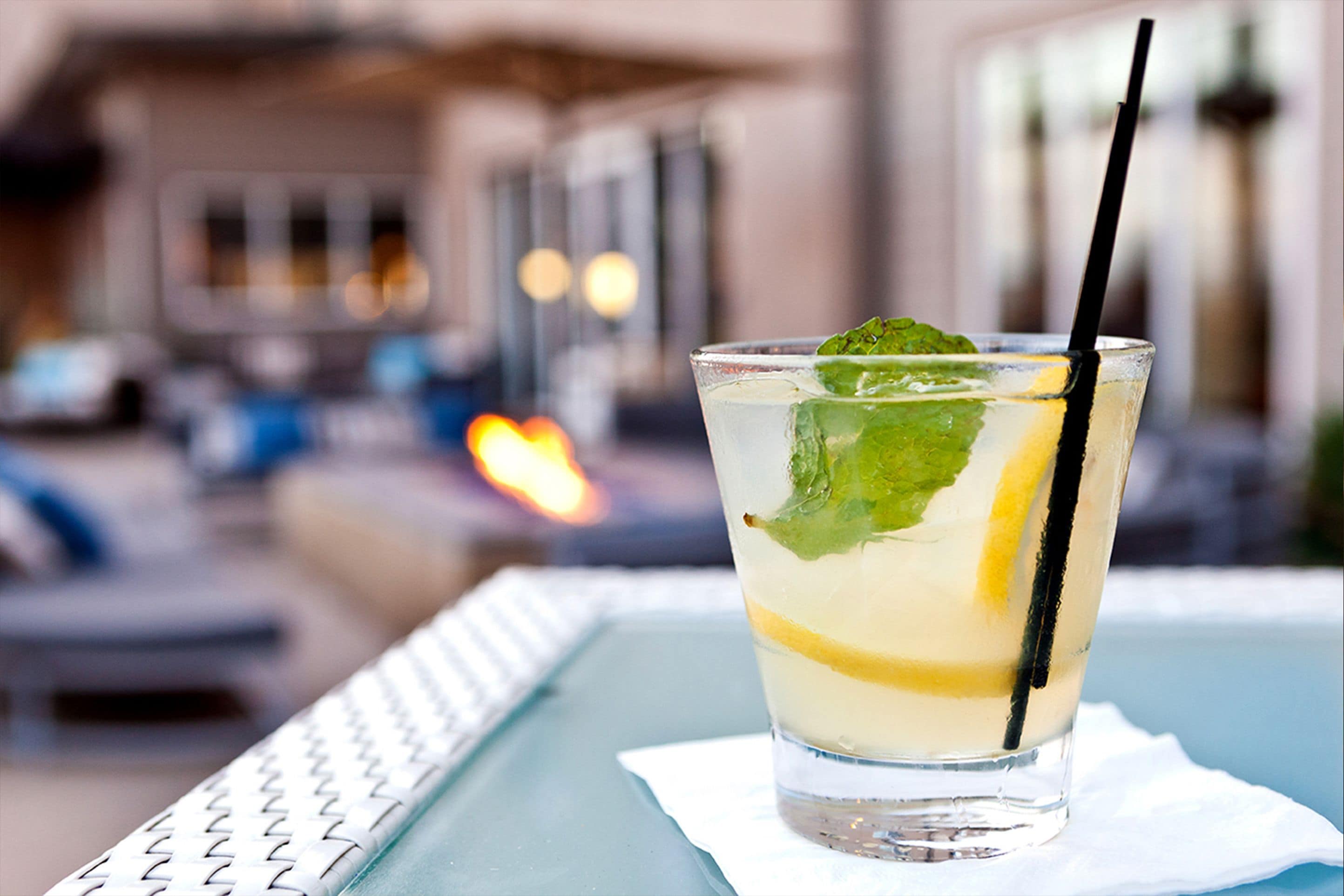 A glass of a clear beverage with a lemon slice and mint garnish on a table with a white napkin.