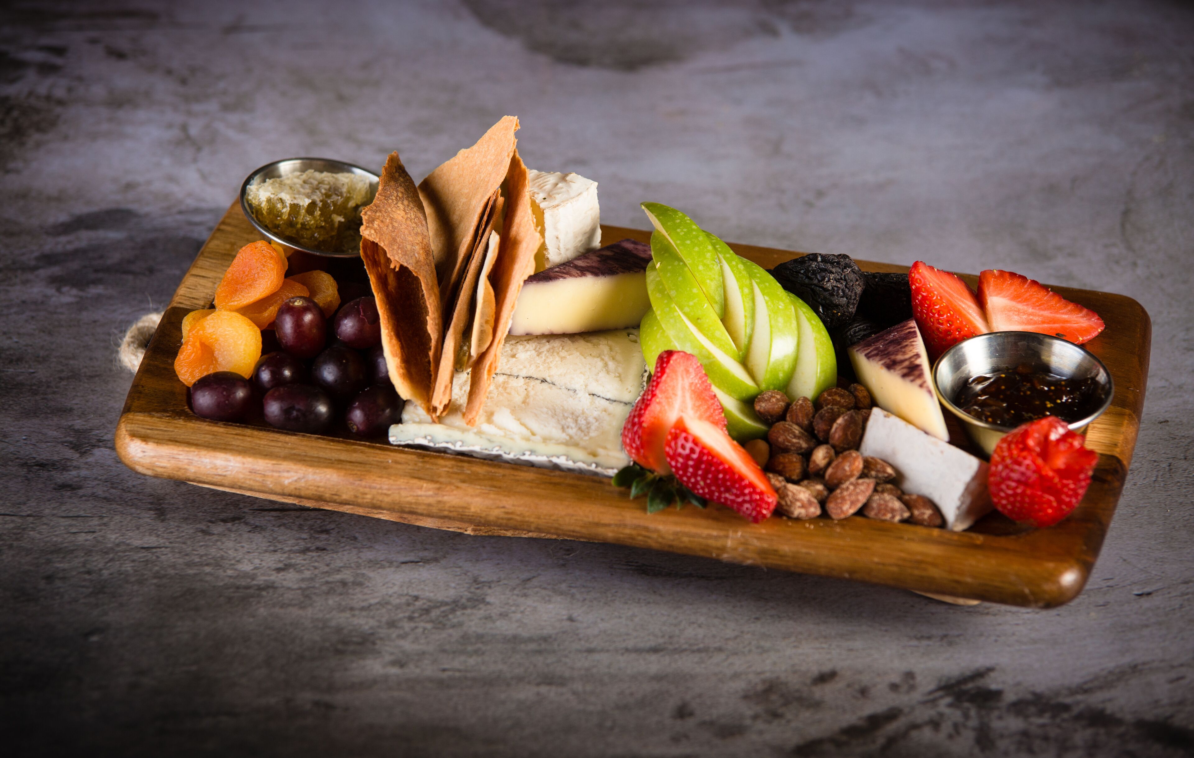 A wooden board with various fruits, cheeses, and nuts.