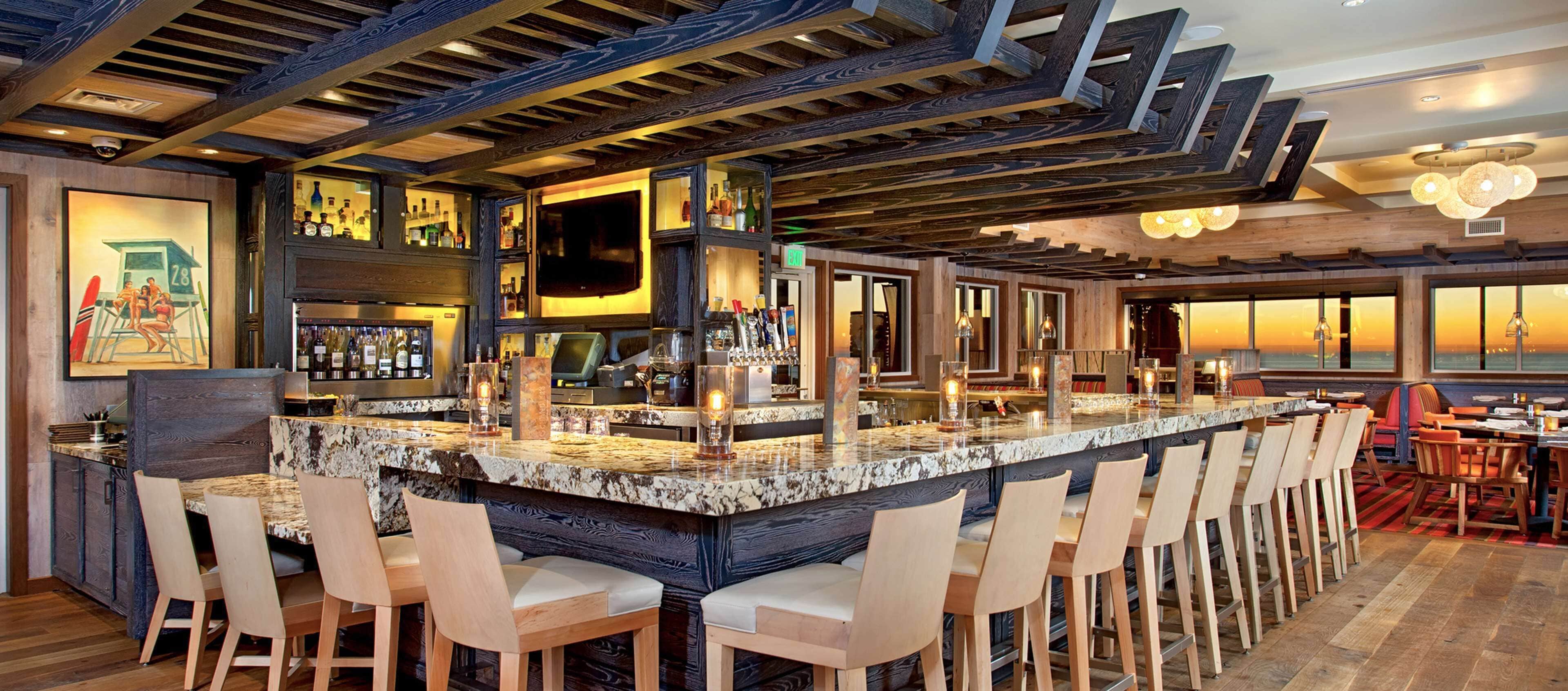 A bar area with a large island, bar stools, and a wooden ceiling.