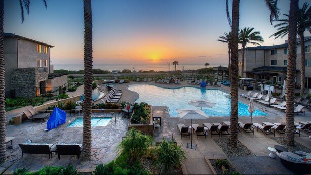 A resort pool area with lounge chairs, umbrellas, and palm trees. - Cape Rey Carlsbad Beach, a Hilton Resort & Spa (Carlsbad)