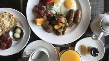 Une table dressée pour le petit-déjeuner, avec des assiettes d’œufs, de saucisses, de pain grillé et des fruits, ainsi qu’une tasse de café et un verre de jus d’orange.