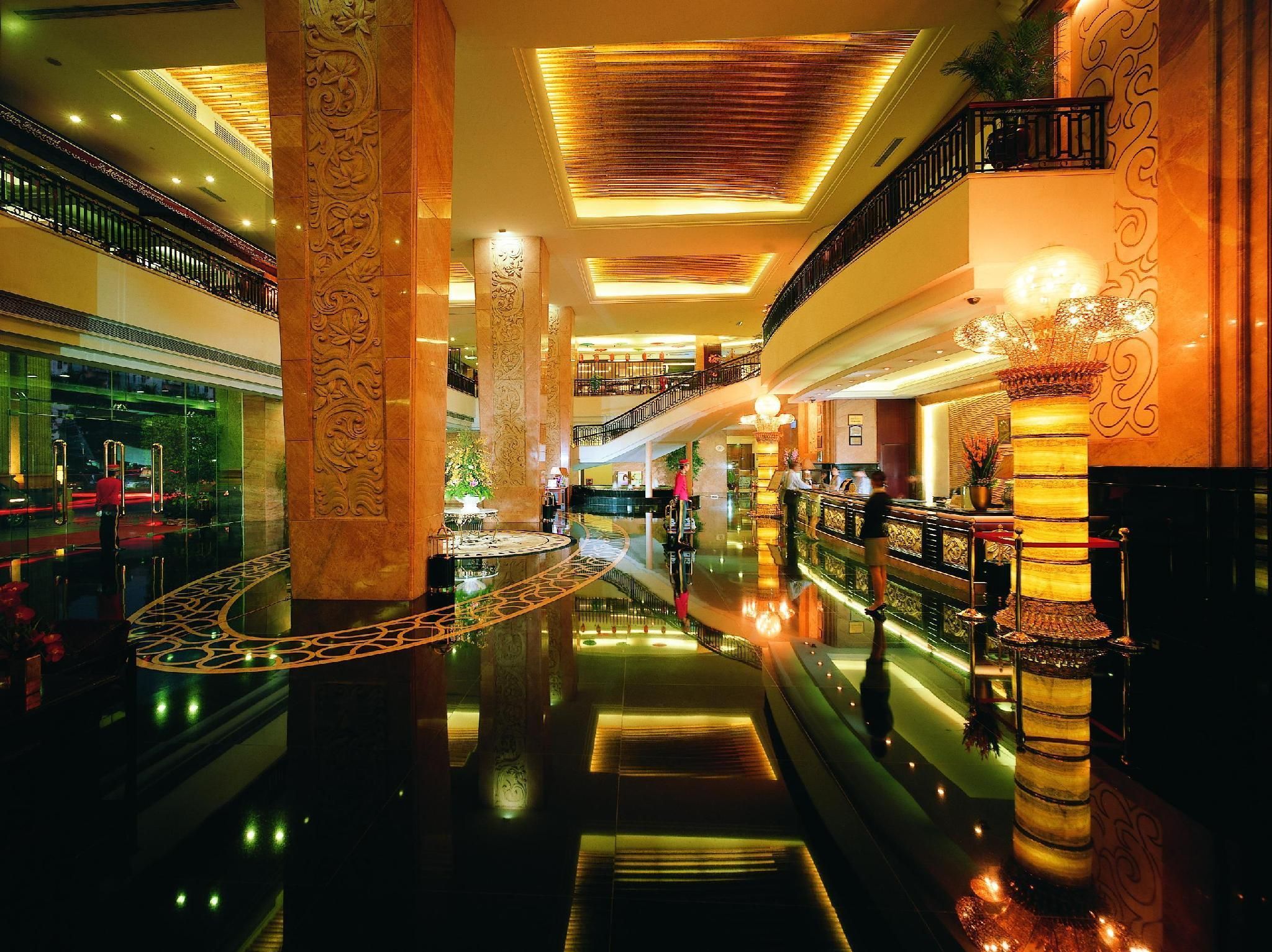Un vestíbulo de hotel de varios niveles con columnas ornamentales, un suelo reflectante y una escalera central.