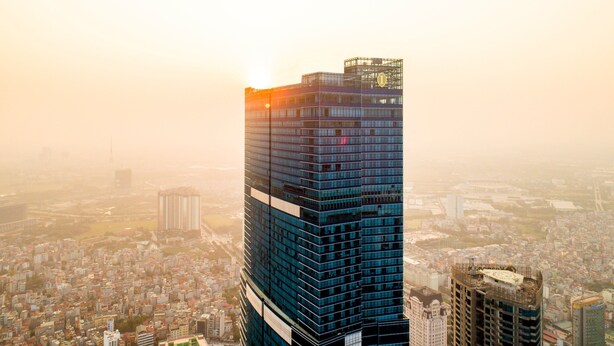 Un edificio de gran altura con fachada de vidrio moderna, rodeado de una zona urbana densa.