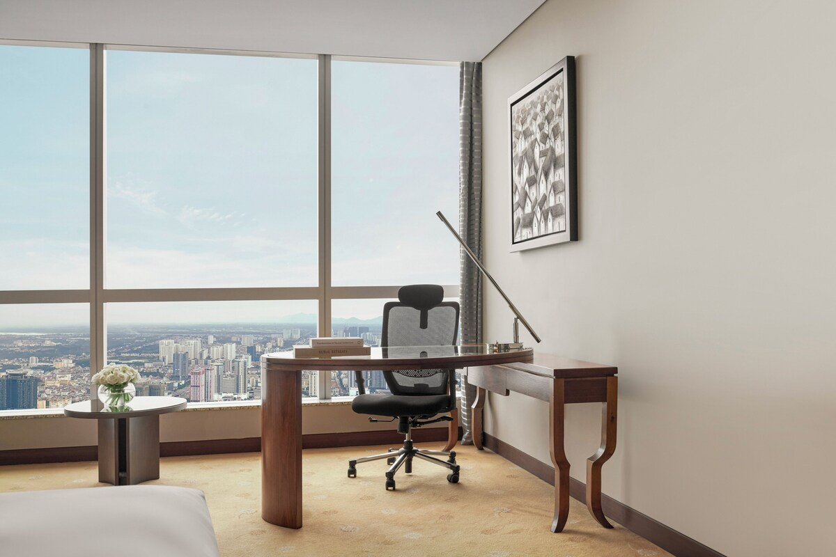 Un espacio de oficina moderno con un ventanal grande, un escritorio, una silla y un jarrón con flores.