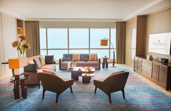 Une chambre d’hôtel spacieuse dotée d’une grande fenêtre, d’un canapé, de deux fauteuils, d’une table basse et d’un téléviseur.