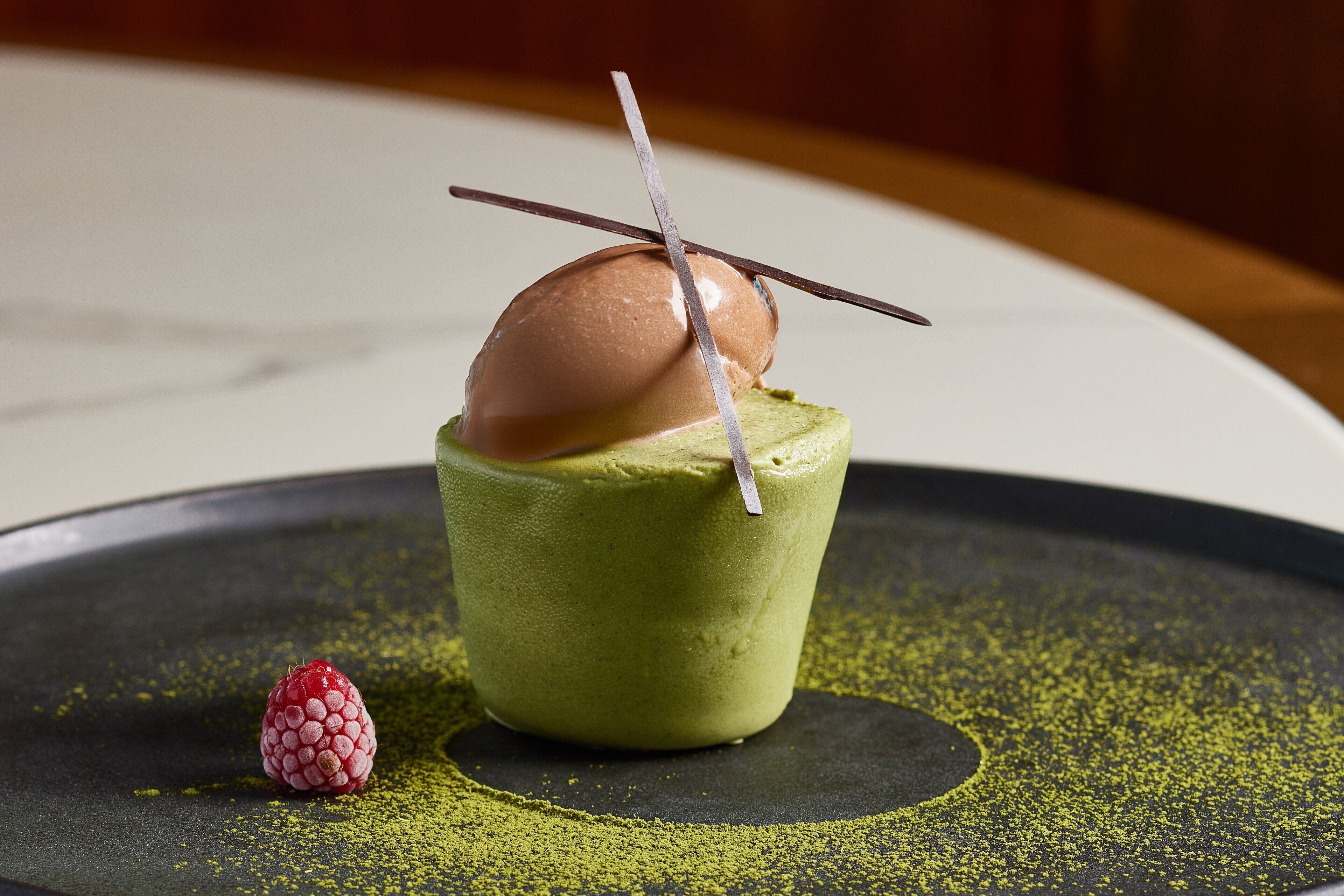 A dessert on a plate with a raspberry and a decorative element.