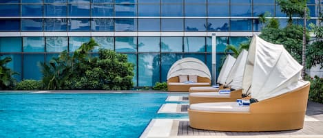 A poolside area with lounge chairs and a modern building with reflective glass windows.