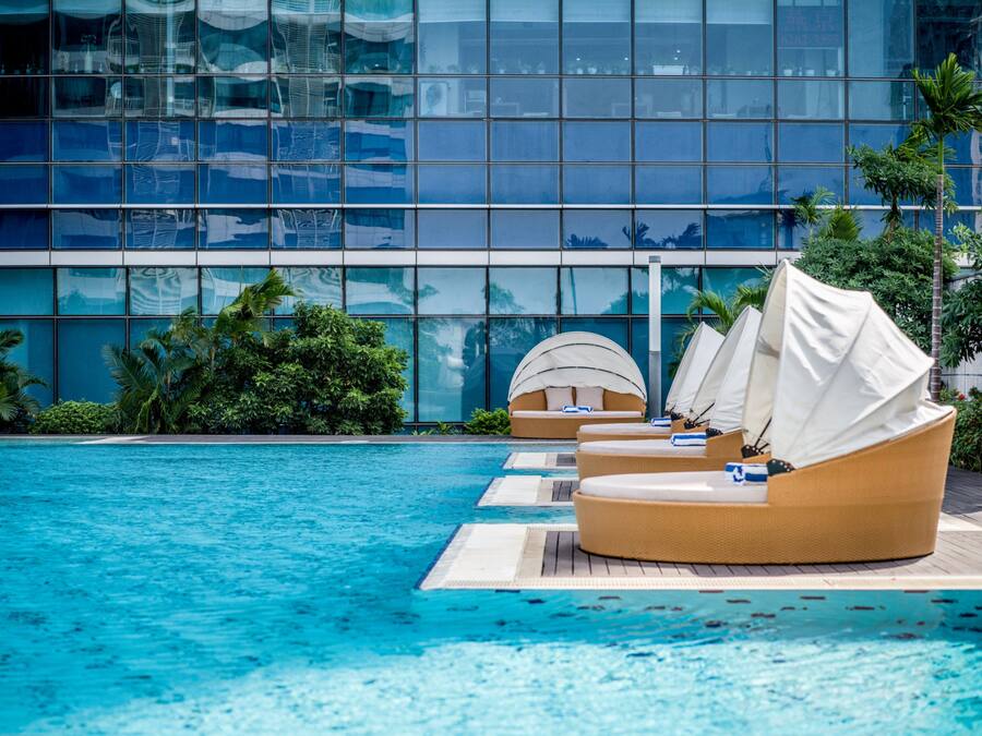 A poolside area with lounge chairs and a modern building with reflective glass windows.