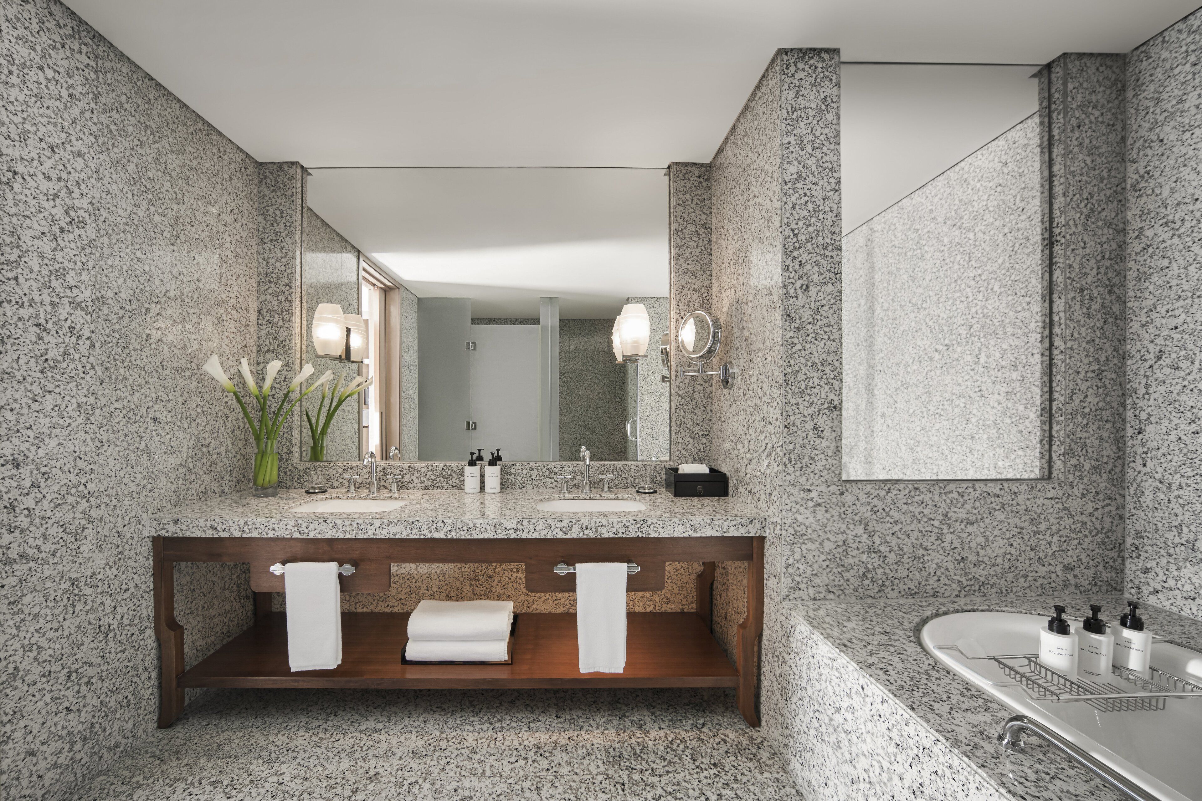 A modern bathroom with granite countertops, a wooden vanity, a large mirror, and a bathtub.