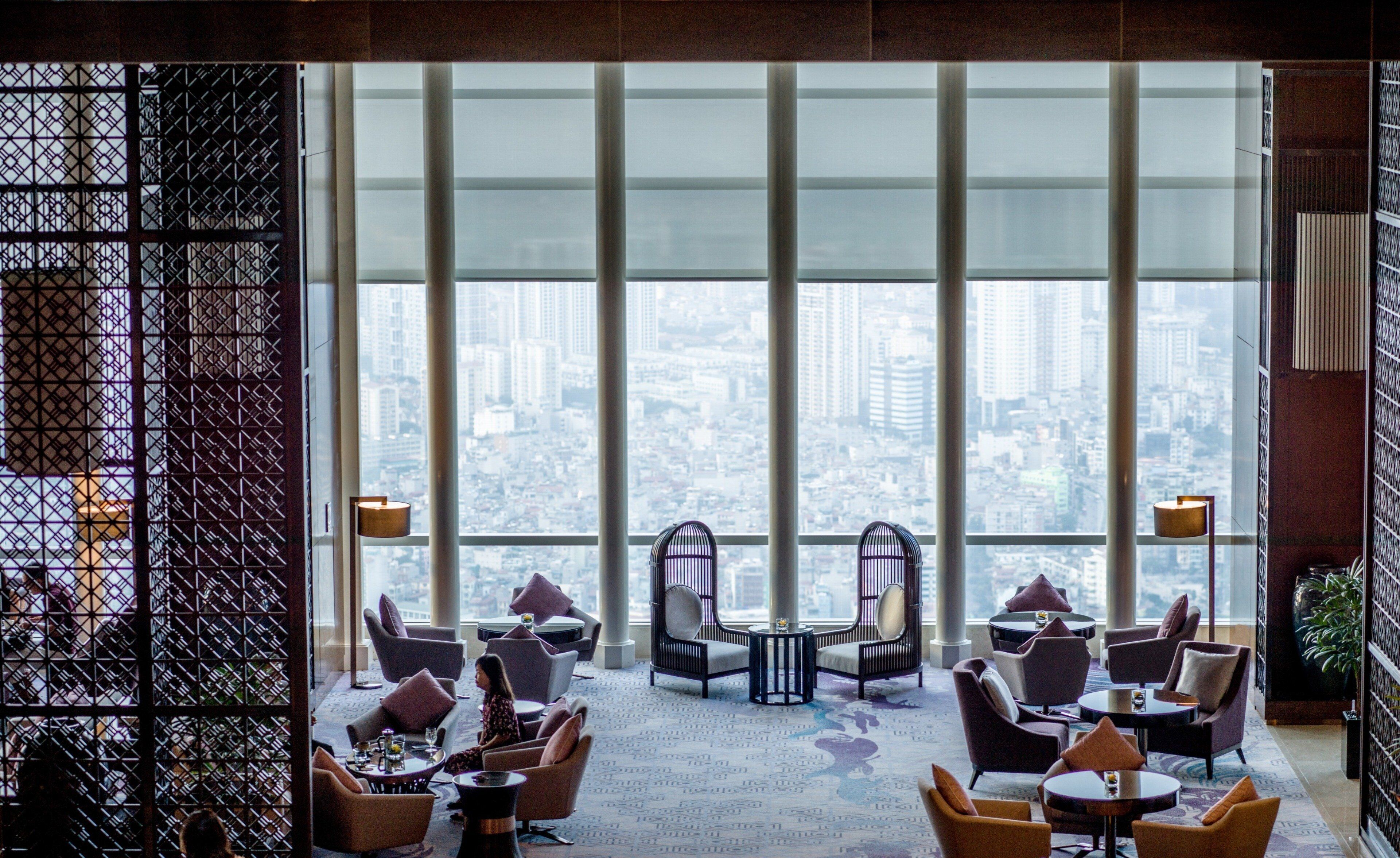 A modern lounge with a city view, featuring multiple seating areas and a large window.
