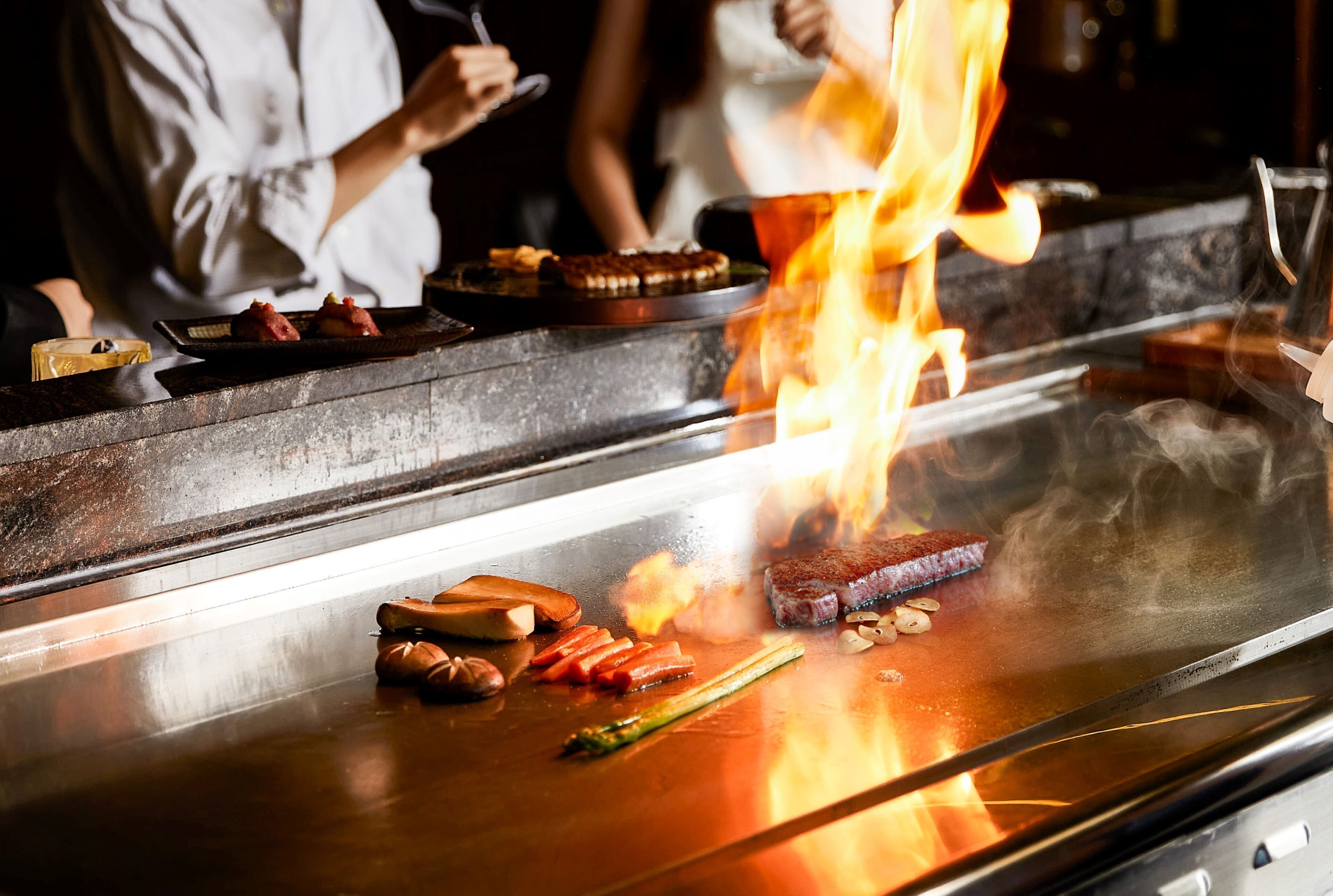 A cooking station with various meats and vegetables being grilled over an open flame.