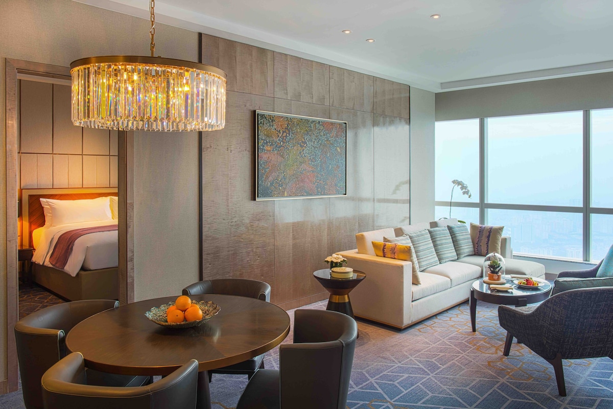 Een moderne hotelkamer met een bed, een zithoek met tafel en stoelen, een bank en een groot raam met uitzicht op de stad.