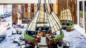Un vestíbulo amplio con arreglos de asientos modernos, una estructura decorativa central y una zona de bar al fondo.