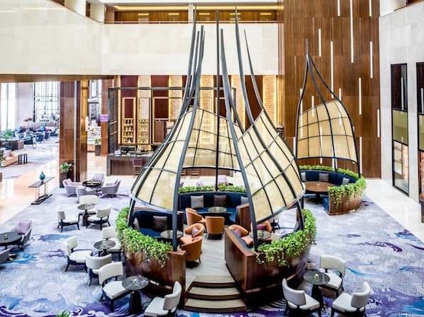Un vestíbulo amplio con arreglos de asientos modernos, una estructura decorativa central y una zona de bar al fondo.