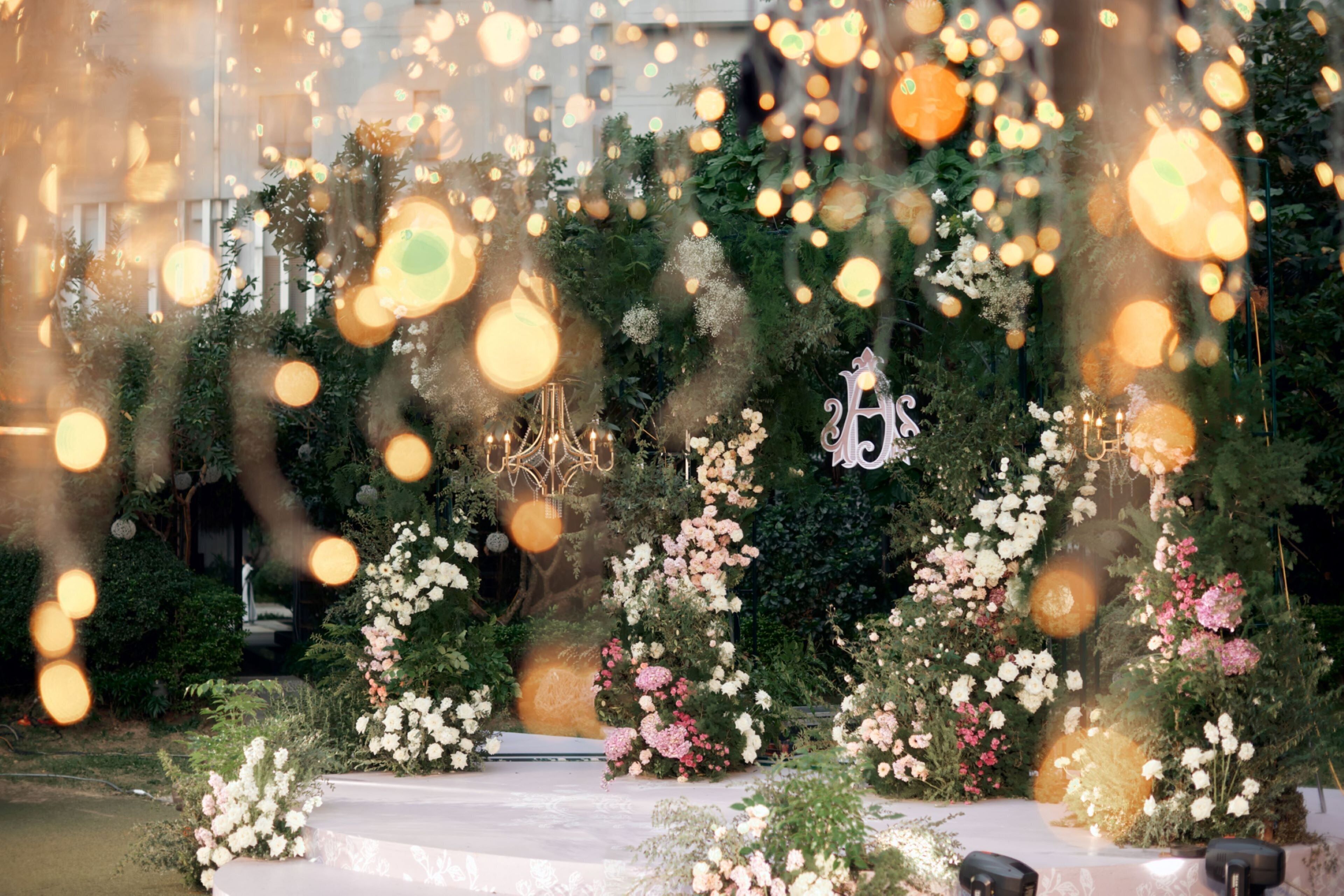 A garden setting with a white table and chairs, surrounded by lush greenery and floral arrangements.
